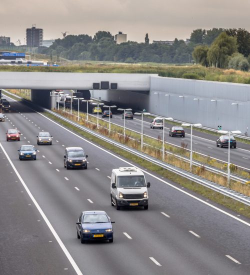 Afternoon traffic on A4 motorway near The Hague Randstad area. Highway crossing aquaduct tunnel with urban area of Rotterdam in backdrop, Netherlands.